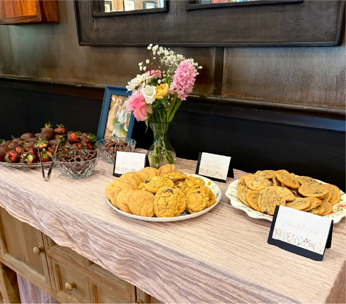Dessert table featuring chocolate chip cookies, white chocolate cranberry macadamia cookies, chocolate-covered strawberries, and fresh flowers at a private event at the Fortin Ironworks Event Lounge